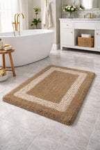 Beige tan Venice rectangular border frame micro polyester bathmat on a modern tiled bathroom floor.