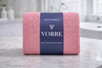 Packaged deep coral pink Vorre Blush microfiber bath towel neatly folded and wrapped with a dark blue luxury brand band.