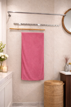 Soft coral pink Vorre Classic microfiber bath towel, ultra-absorbent quick-drying body sheet on a minimalist luxury wooden stool.