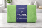 Packaged lime green Vorre Classic microfiber bath towel featuring a dark blue brand sleeve wrapper on a white marble surface.