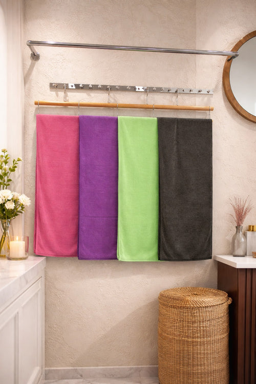 Four colorful Vorre Classic microfiber bath towels in pink, purple, green, and charcoal grey hanging neatly on a modern bathroom towel bar.