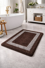 Dark brown Venice border frame micro polyester bathmat with an anti-skid backing next to a white bathtub.