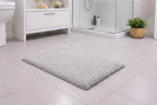 Light silver grey fluffy surface micro polyester bathmat spread on a modern tiled bathroom floor.