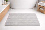 Light grey solid stripe microfiber bath rug, 2000 GSM plush non-slip mat next to a tub.