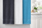 Three-color display of Vorre Micro Border bath towels showcasing charcoal grey, classic white, and turquoise blue variants together.
