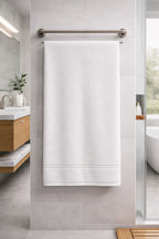 Classic white Vorre Micro Border bath towel, plush 350 GSM micro polyester body towel hanging beautifully in a modern grey-tiled bathroom.