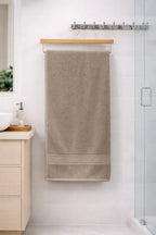 Beige taupe neutral-toned Vorre Norvelle recycled cotton bath towel, durable 400 GSM terry loop fabric body sheet displayed on a wooden hanger.