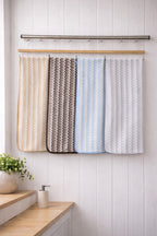 Four assorted colors of Vorre Pure Edge microfiber bath towels with white chevron zig-zag patterns hanging neatly on a modern bathroom rack.