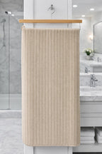 Beige cream textured Vorre Ripped microfiber bath towel, soft lint-free ribbed personal care towel hanging on a wooden hanger.