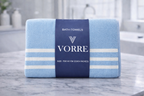 Packaged light blue striped Vorre microfiber bath towel neatly folded and wrapped with a dark blue luxury brand band.